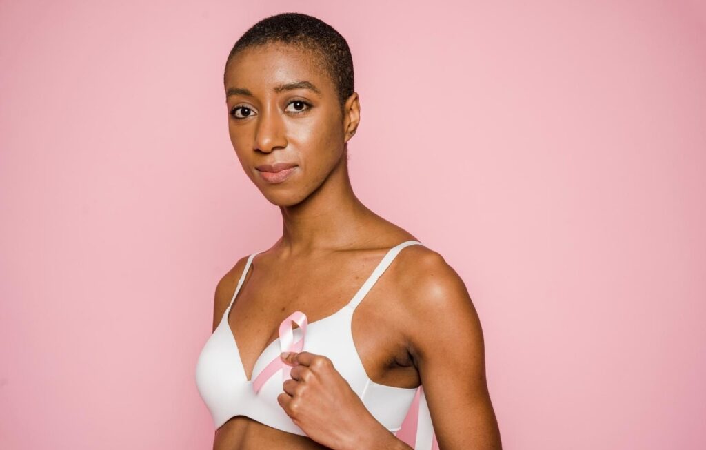 mulher negra segurando um laço rosa em frente ao peito, representando uma pessoa negra com câncer de mama e as disparidades raciais da doença