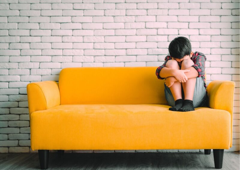criança encolhida no canto de um sofá amarelo, triste, representando a saúde mental infantil
