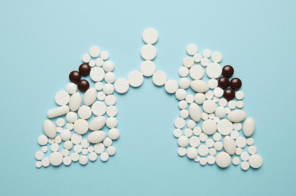 comprimidos brancos em formato de pulmão, com comprimidos mais escuros representando focos de tuberculose, representando o tratamento da tuberculose pulmonar