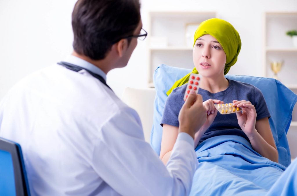 paciente com câncer em hospital segurando comprimidos de inlunestranto e conversando com o médico sobre efeitos adversos