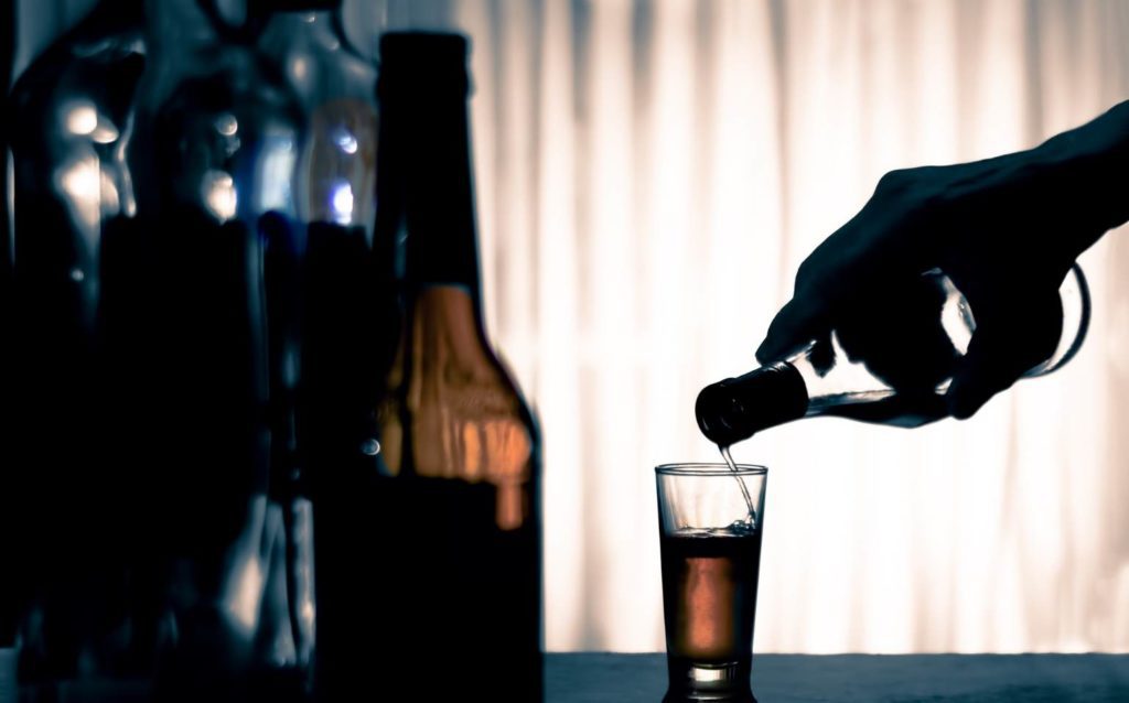 pessoa servindo dose de bebida alcoólica, representando o alcoolismo