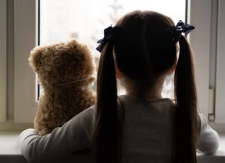 Saúde mental infantil: os efeitos da pandemia ainda estão presentes? criança com ursinho de pelúcia, de costas, parecendo triste, representando a saúde mental infantil