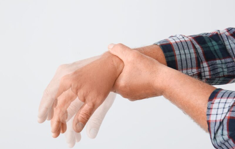 paciente com tremor e movimentos involuntários das mãos, segurando o punho, podendo indicar síndrome extrapiramidal