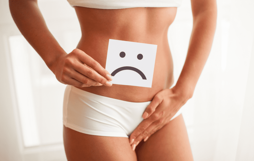 mulher segurando placa com rosto triste em frente a vagina, representando Vulvovaginites e Vaginoses