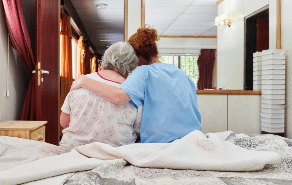 paciente idosa sentada na cama, sendo acolhida por profissional de saúde, por apresentar síndromes geriátricas
