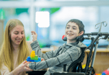 FDA aprova apitegromab (Isembyld): primeira terapia muscular para AME criança sorrindo, ao lado da cuidadora, em cadeira de rodas com atrofia muscular espinhal, que pode ser tratada com Apitegromab (Isembyld).