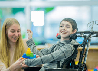 FDA aprova apitegromab (Isembyld): primeira terapia muscular para AME criança sorrindo, ao lado da cuidadora, em cadeira de rodas com atrofia muscular espinhal, que pode ser tratada com Apitegromab (Isembyld).