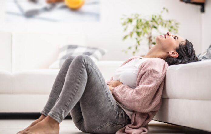 mulher sentada no chão, com sinais de irritação e dor abdominal, um possível sintoma de transtorno disfórico pré-menstrual (TDPM)