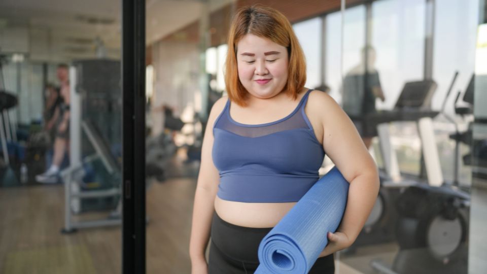 mulher segurando tapete de yoga, avaliando benefícios da yoga para obesidade