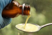 Anvisa proíbe xaropes com Clobutinol após risco de arritmia grave Xarope sendo derramado em colher, representando suspensão de medicamentos com Clobutinol pela Anvisa por risco de arritmia grave.