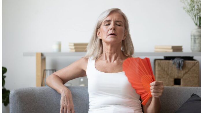 mulher se abanando com leque por conta dos sintomas vasomotores da menopausa, que podem ser amenizados com fezolinetanto aprovado pela Anvisa