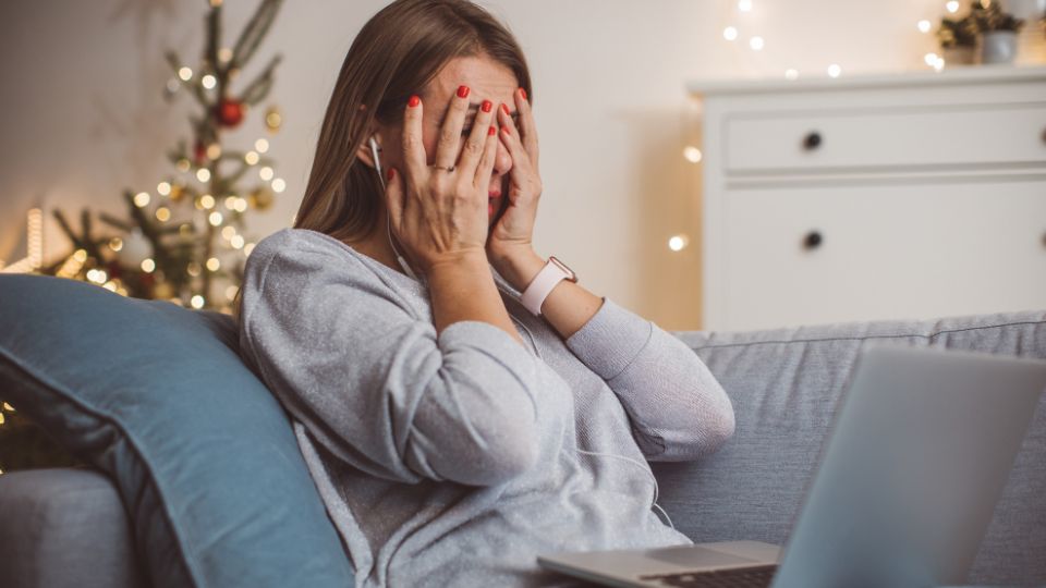 mulher com as mãos no rosto, sentada, com o computador no colo, representando uma mulher sobrecarregada recebendo atendimento psicológico gratuito pelo teleatendimento pelo SUS