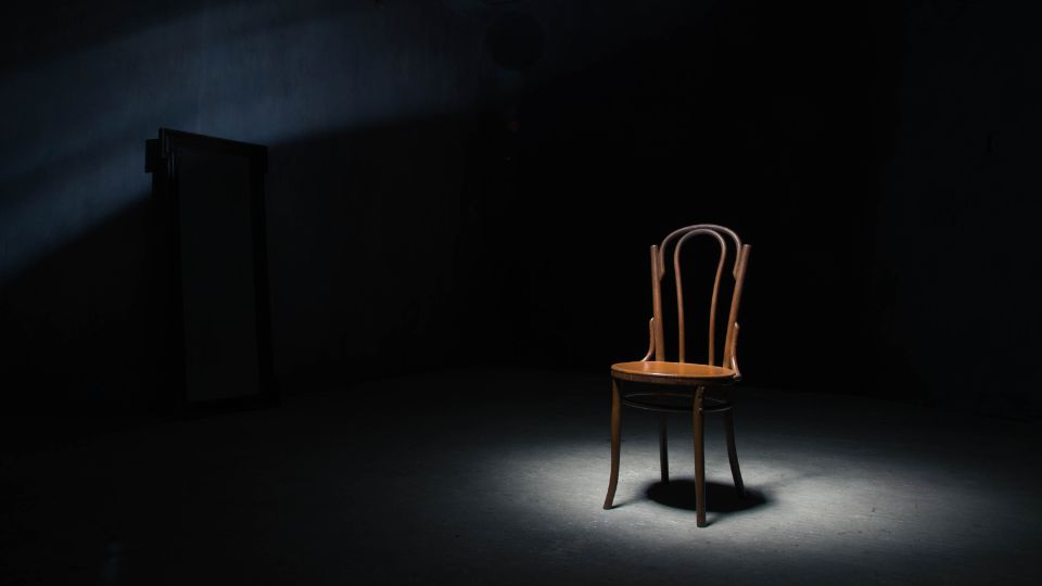 imagem de uma cadeira vazia no escuro, composição minimalista que simboliza ausência e perda no contexto da violência contra a mulher.